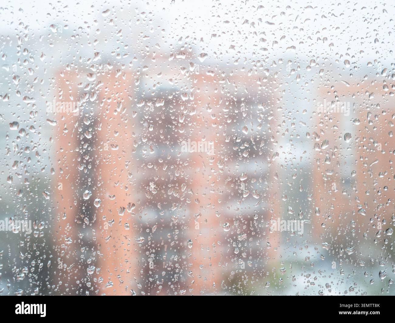 gocce d'acqua dalla pioggia e neve sciolta sulla superficie in vetro della finestra della casa e condomini sfocati sullo sfondo Foto Stock