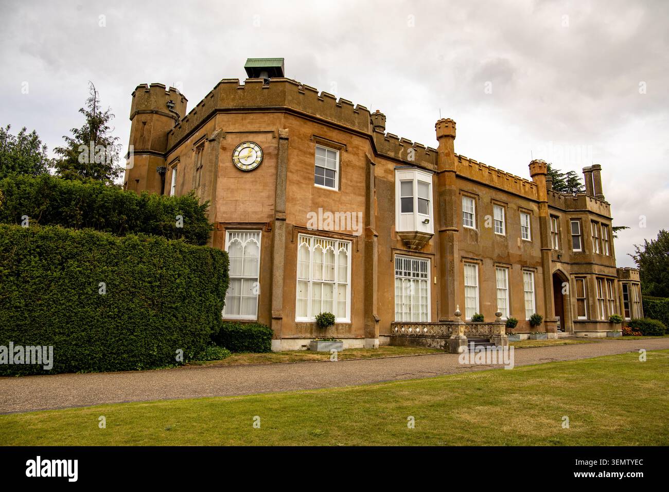 Vista ad angolo basso della casa di Nonsuch Mansion con merlature e un orologio sulla facciata circondato da siepi ben curate e erba verde Foto Stock