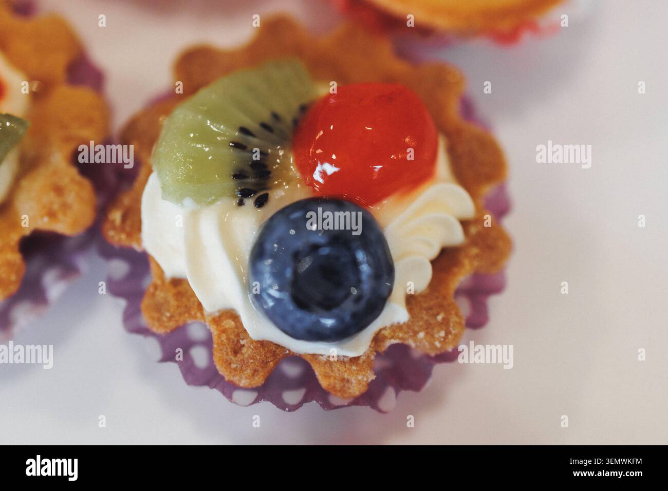 Crostata delicata con panna montata e frutta colorata. Kiwi, ciliegia e mirtillo creano un'atmosfera vivace. La crosta dorata culla dolce e fresca Foto Stock