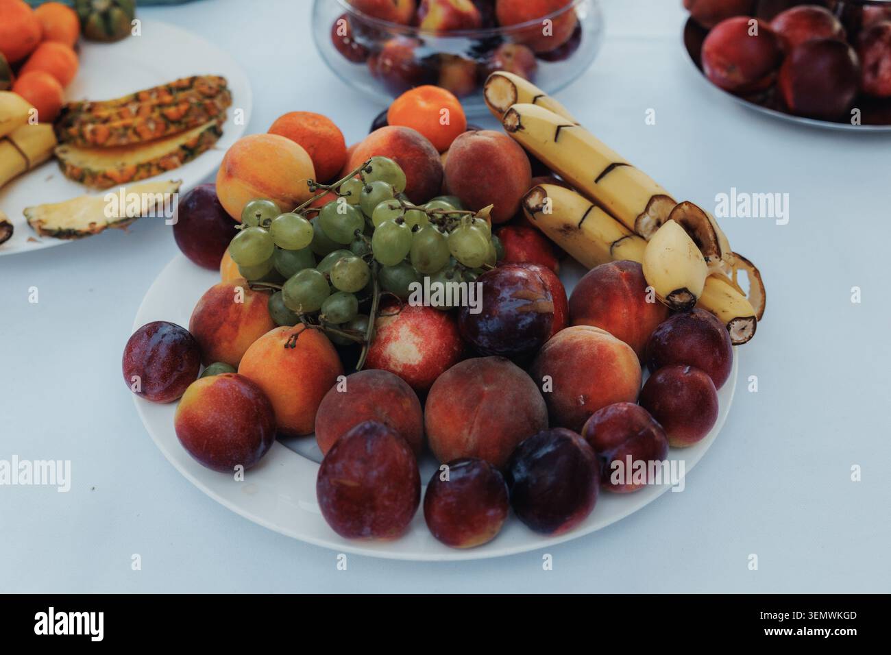 Un piatto di frutta colorata invita alla freschezza e alla gioia. Prugne, uva, pesche e banane riempiono il piatto. I toni vivaci suggeriscono un pasto sano e allegro. P Foto Stock