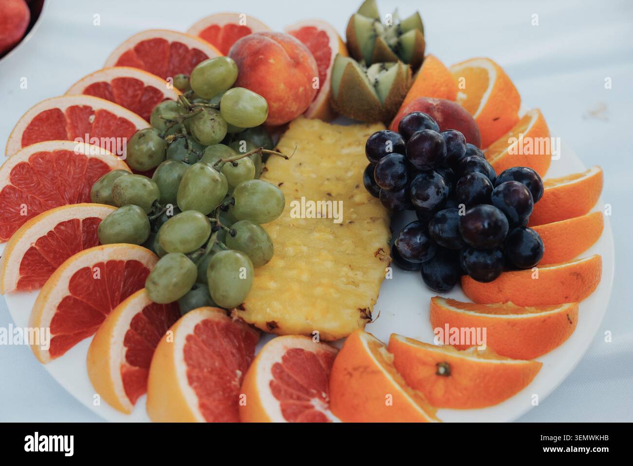 Frutta fresca disposta a pianta circolare. Grappoli di uva, arance e una fetta di ananas. Le fette di pompelmo rosse e rosa aggiungono contrasto. Colorato, vib Foto Stock