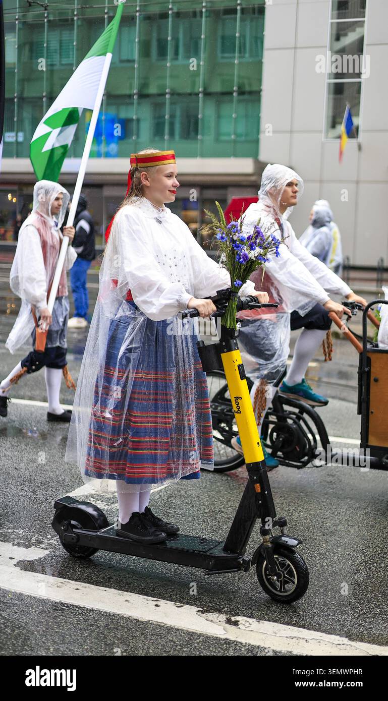Tallinn, Estonia - 5 luglio 2025: Donna in costume popolare estone cavalca uno scooter elettrico con fiori selvatici durante la parata della celebrazione della canzone e della danza Foto Stock