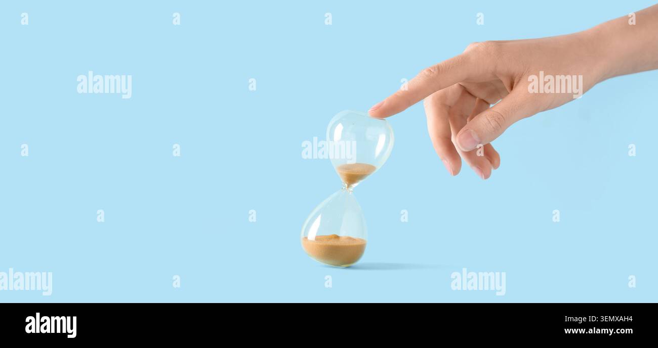 Mano umana che tocca la clessidra, gestione del tempo e concetto di scadenza, tempo di passaggio e urgenza, isolato su sfondo blu Foto Stock