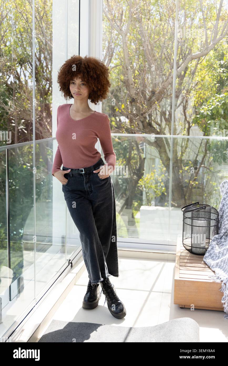 Donna afroamericana a metà anni '20 in piedi davanti a finestre di vetro con ringhiera di vetro, con rosone e stivali Foto Stock