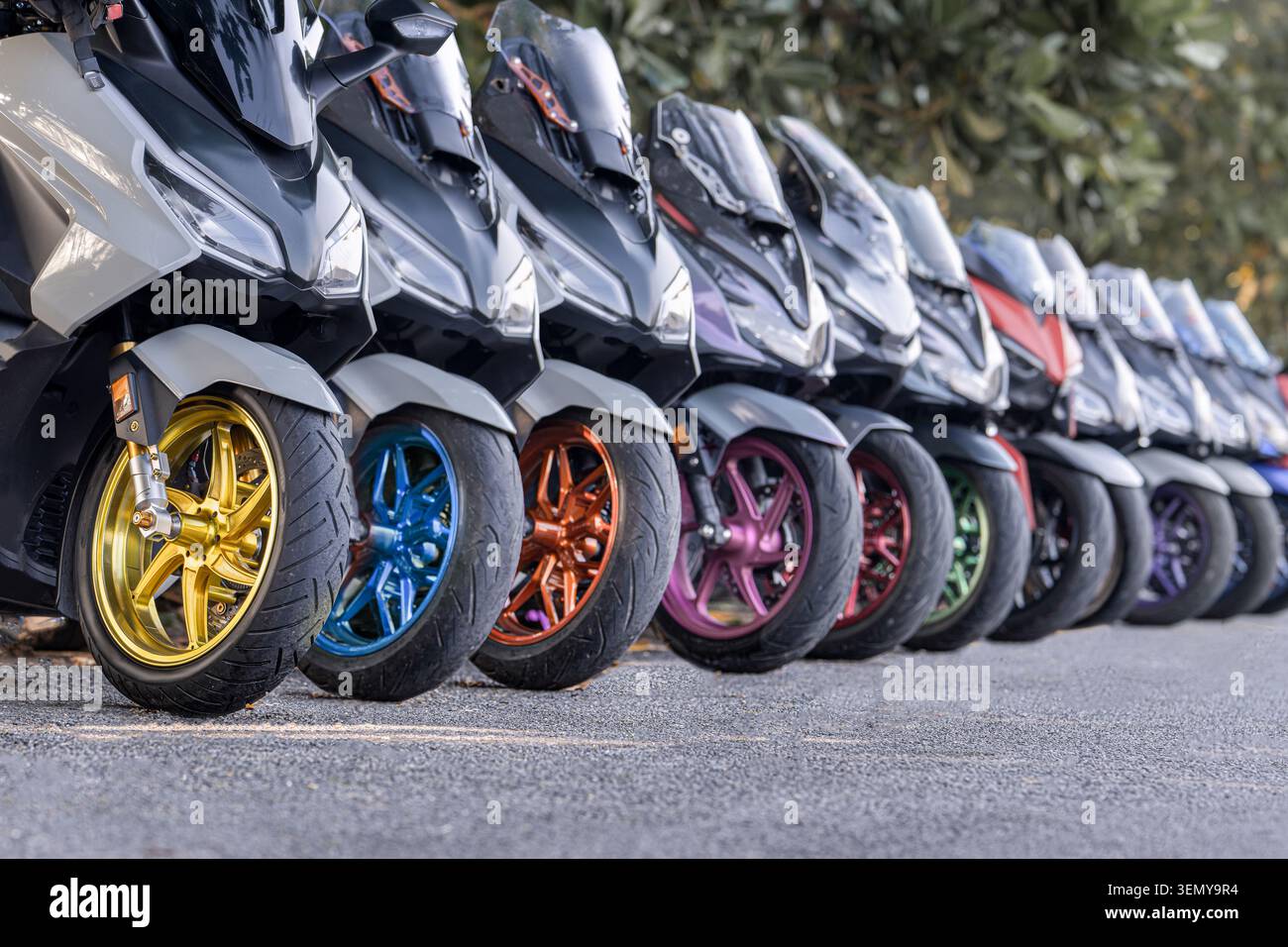 Linea di scooter moderni con ruote colorate e personalizzate parcheggiate sulla strada. Concetto di noleggio scooter, mobilità urbana, viaggio e trasporto. Popula Foto Stock