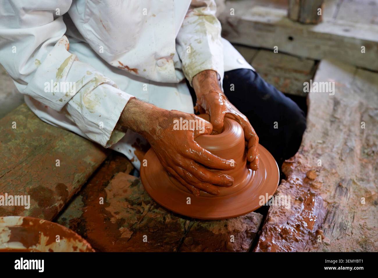 Potter lavora una grande massa di argilla bagnata su una ruota rotante, dimostrando le tecniche e l'artigianato tradizionali della ceramica. Foto Stock