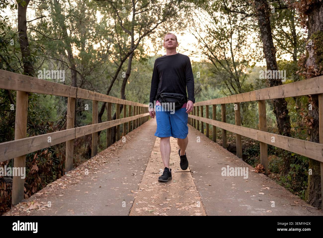Uomo che cammina su una passerella naturalistica in una foresta con pantaloncini corti e un pacchetto fanny Foto Stock