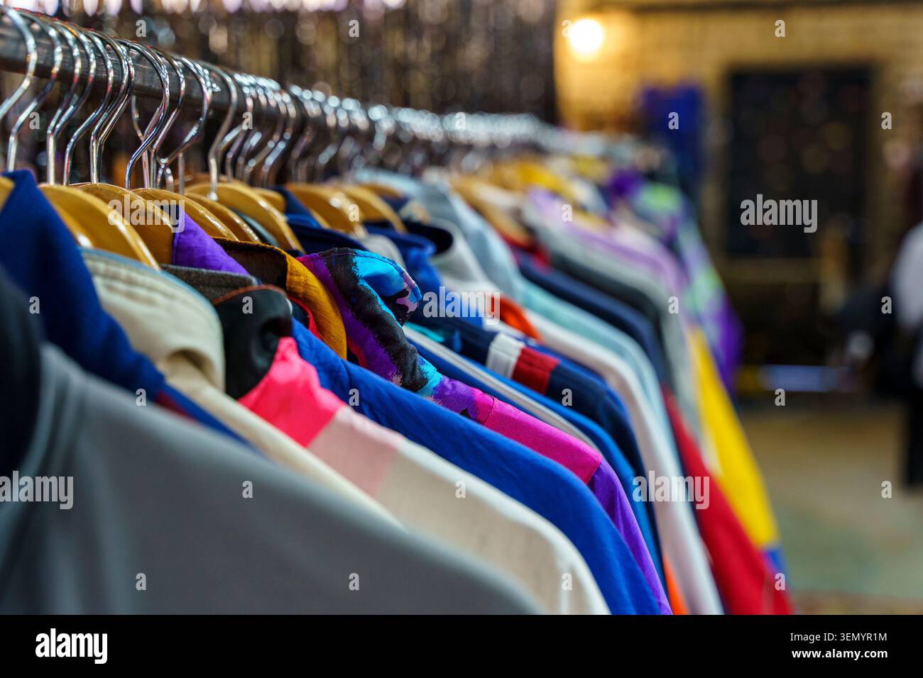 Varieta' colorata di abbigliamento vintage e abiti di seconda mano appesi su un rack in un negozio o mercato delle pulci. Questa immagine cattura il concetto di moda sostenibile, stile retrò e l'esperienza di caccia al tesoro dello shopping di capi usati unici. Foto Stock