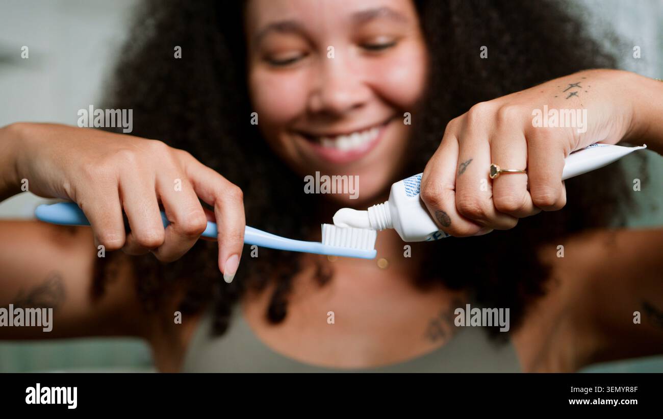 Donna nera sorridente che stringe il dentifricio sullo spazzolino durante la routine di igiene mattutina a casa Foto Stock