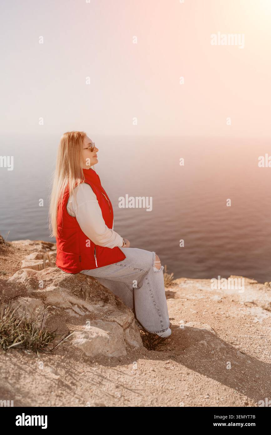 Donna con scogliera che siede su una sporgenza rocciosa che si affaccia sull'oceano durante una luminosa giornata di sole con spazio fotocopie Foto Stock