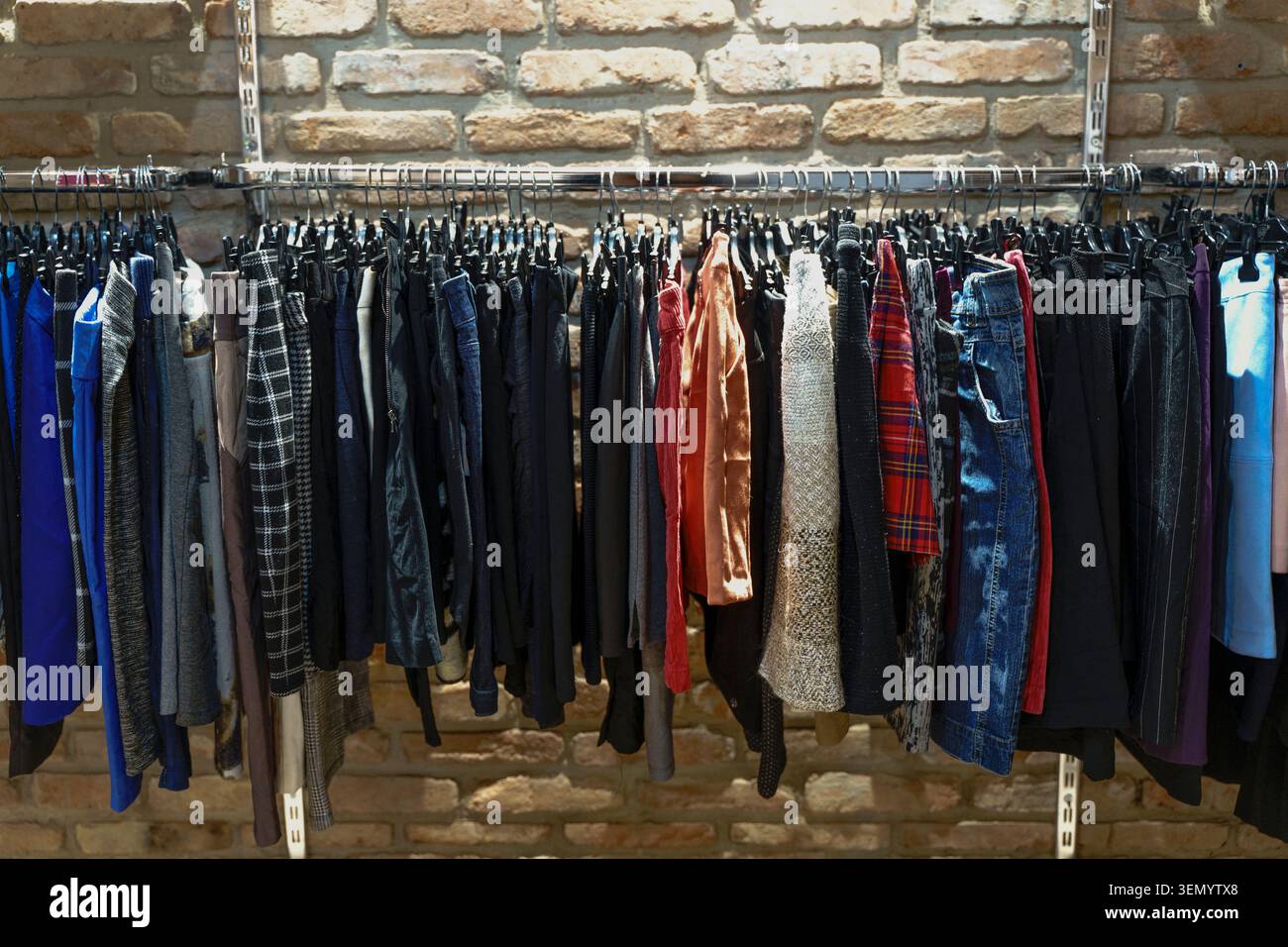 Varieta' colorata di abbigliamento vintage e abiti di seconda mano appesi su un rack in un negozio o mercato delle pulci. Questa immagine cattura il concetto di moda sostenibile, stile retrò e l'esperienza di caccia al tesoro dello shopping di capi usati unici. Foto Stock