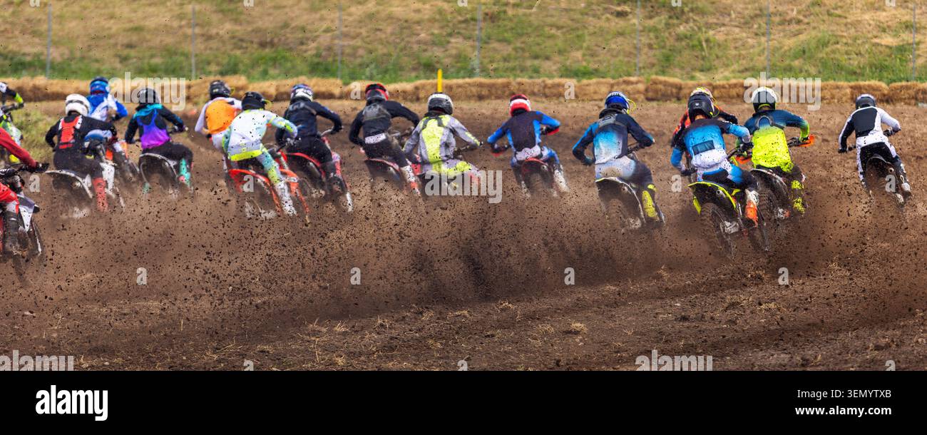 I motociclisti di Motocross guardano indietro su moto da terra prima di iniziare una gara competitiva su pista all'aperto. Attrezzature protettive per le macchine coperte di fango per gli atleti creano atmosfera Foto Stock