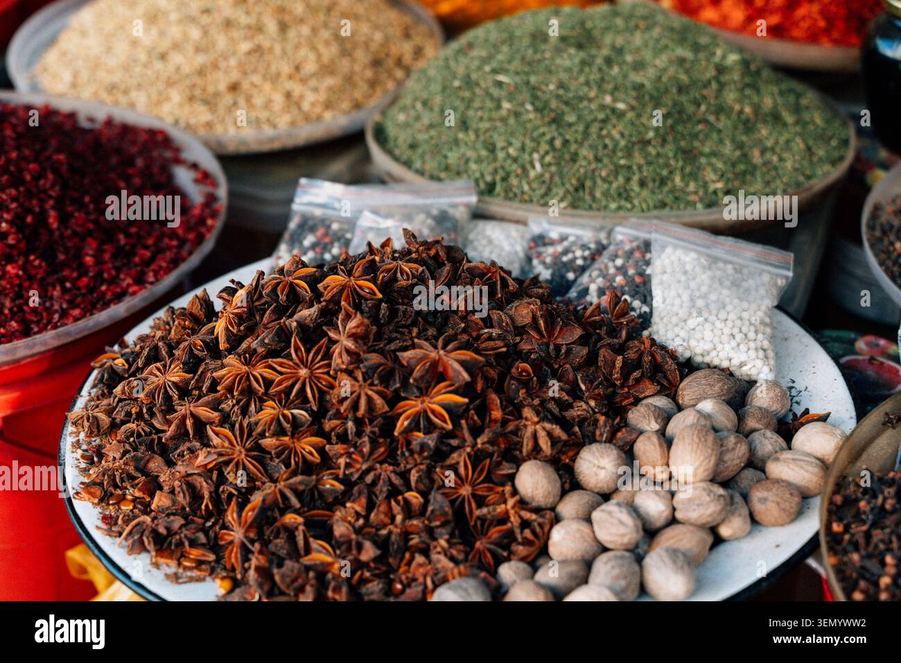 Una vivace e aromatica esposizione di varie spezie, tra cui anice stellato, noce moscata ed erbe macinate colorate, disposte in grandi ciotole e piccoli sacchetti. Questa immagine mostra le ricche tradizioni culinarie di un autentico mercato orientale o bazar. Foto Stock