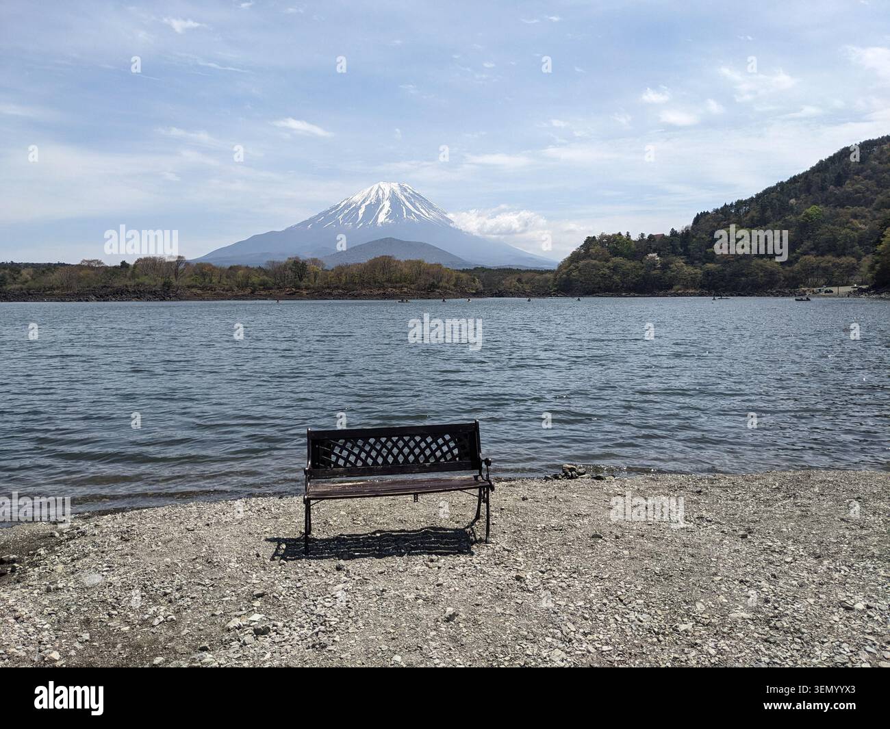 Momento tranquillo vicino al lago, una panchina solitaria che si affaccia sulla cima innevata mozzafiato del Monte Fuji sotto un cielo blu. Foto Stock