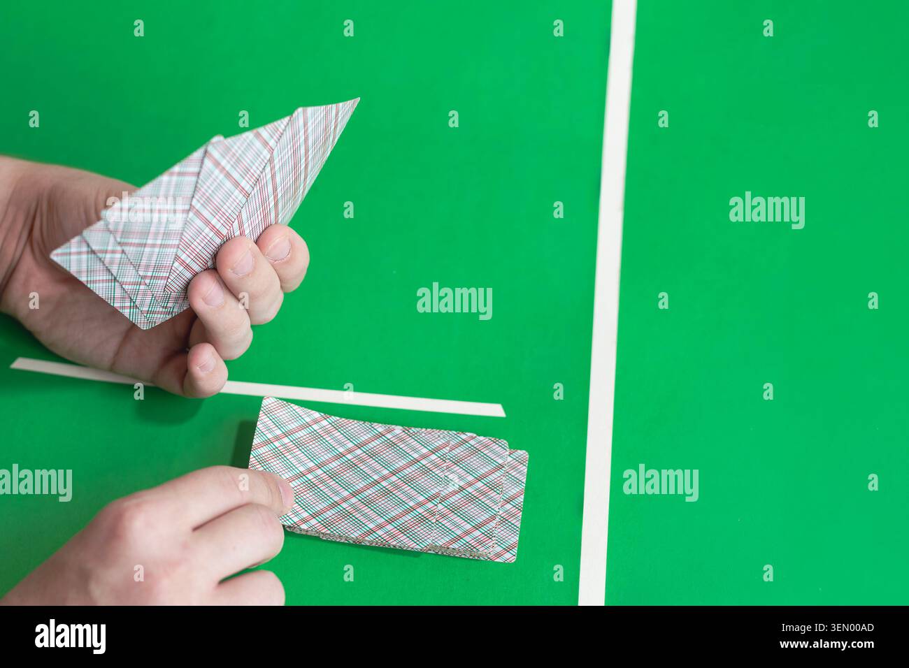 Le mani distribuiscono le carte da gioco con i dorsi a quadri su un tavolo verde con linee bianche. La mano sinistra tiene la ventola delle carte, la mano destra prende la carta dal mazzo. Dita e pa Foto Stock