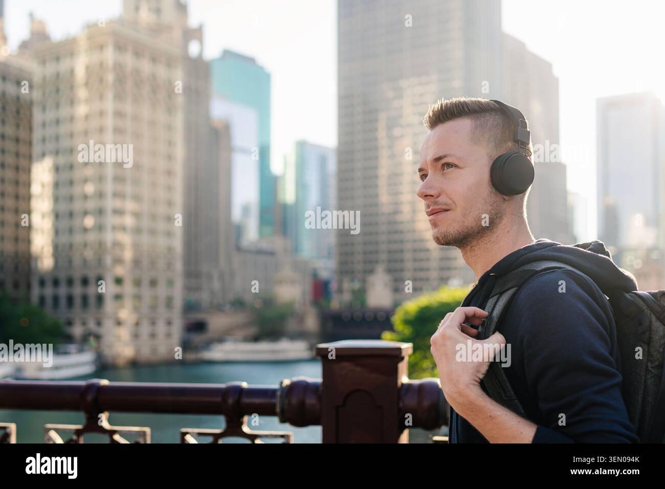 Ritratto di un uomo medio adulto con le cuffie che cammina sul lungomare nel centro di Chicago durante il giorno. Stile di vita urbano, tecnologia audio moderna, musica di città Foto Stock