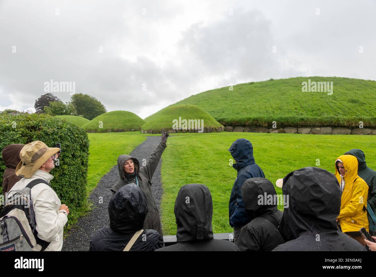 La guida del tour parla sotto la pioggia ai visitatori della tomba di passaggio neolitica di Knowth, Boyne Valley, Irlanda Foto Stock