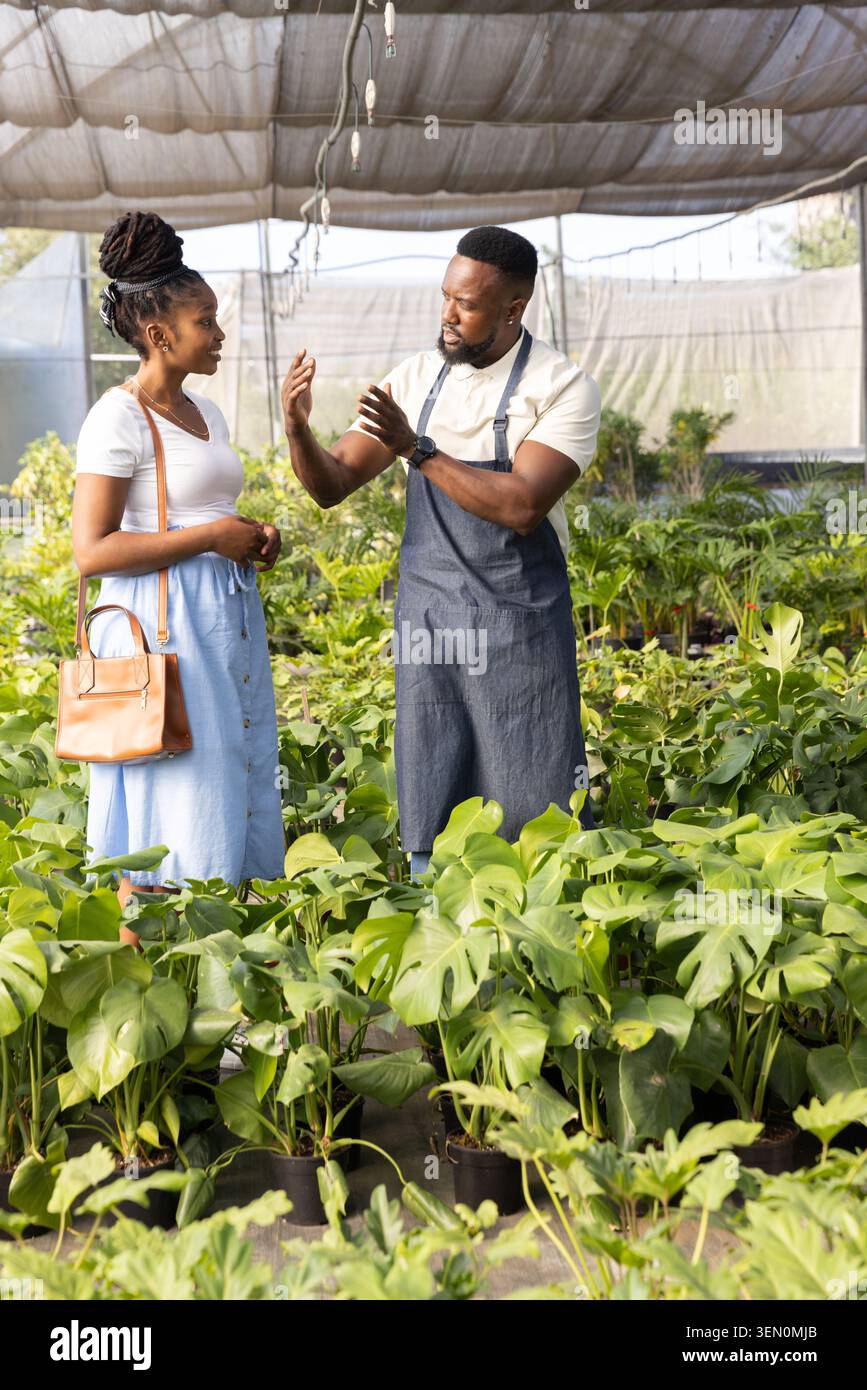 Uomo e donna afro-americana, uomo in grembiule grigio gestante, donna che tiene un sacchetto abbronzante tra le piante Foto Stock