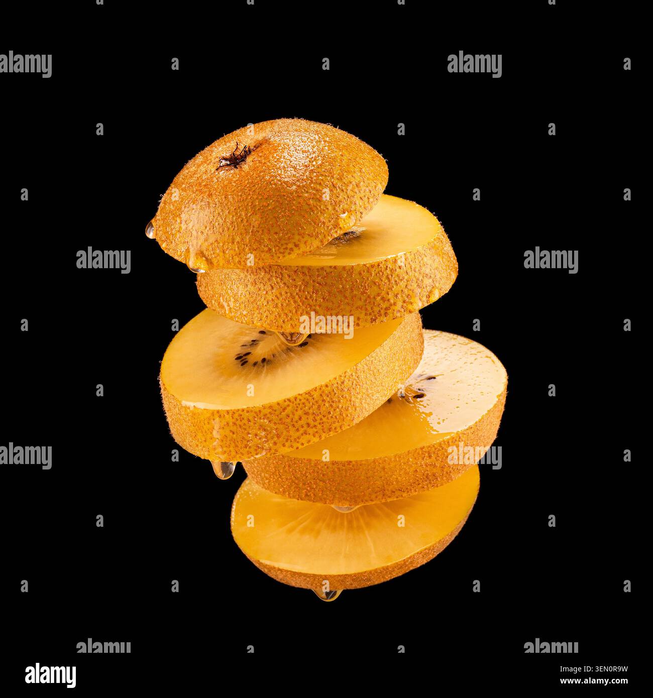 Kiwi dorato intero con fette sovrapposte che mostrano polpa succosa, isolato su sfondo nero con goccioline di succo visibili. Foto Stock