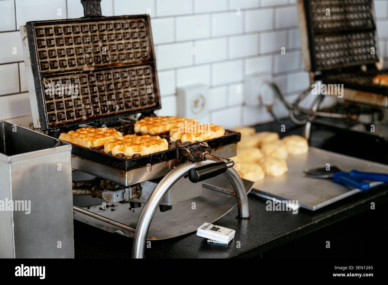 Ferro da stiro per waffle su un piano di lavoro per preparare waffle freschi dorati in cucina. Foto Stock