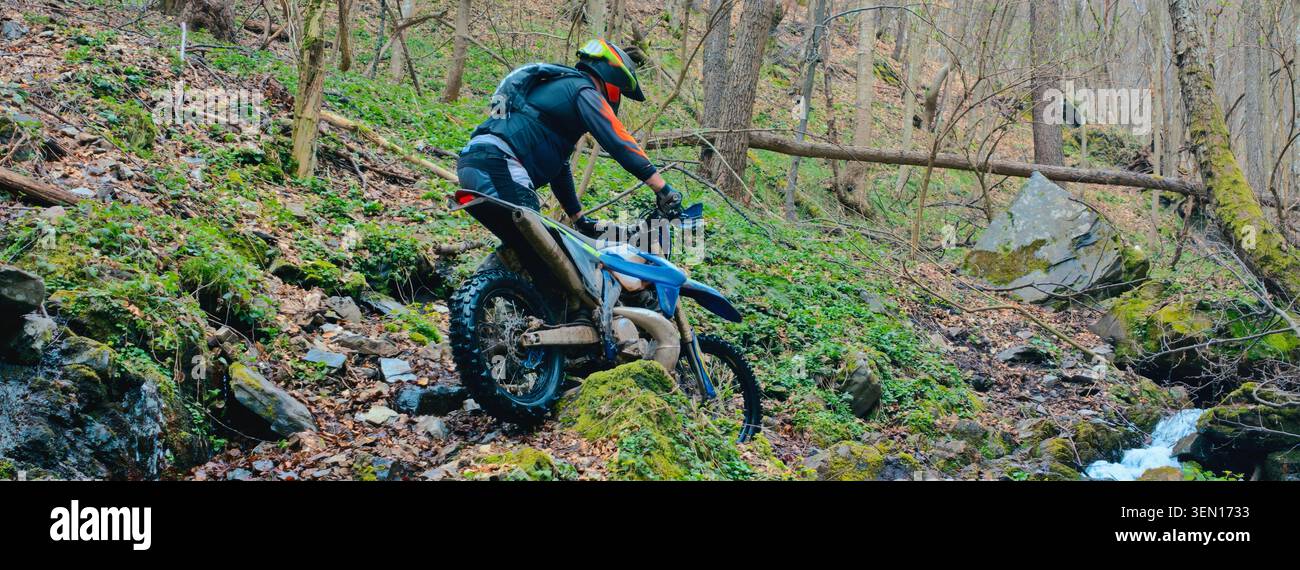 Fuoristrada Dirt Bike Rider navigando lungo il Mossy Forest Trail Stream sulla Mountain Enduro Motorcycle Foto Stock