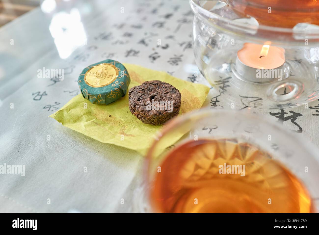 Tè fermentato Jangheung Cheongtaejeon in una pentola di vetro, accanto al suo unico blocco invecchiato a forma di moneta su un panno calligrafico, che mostra la cultura asiatica. Foto Stock