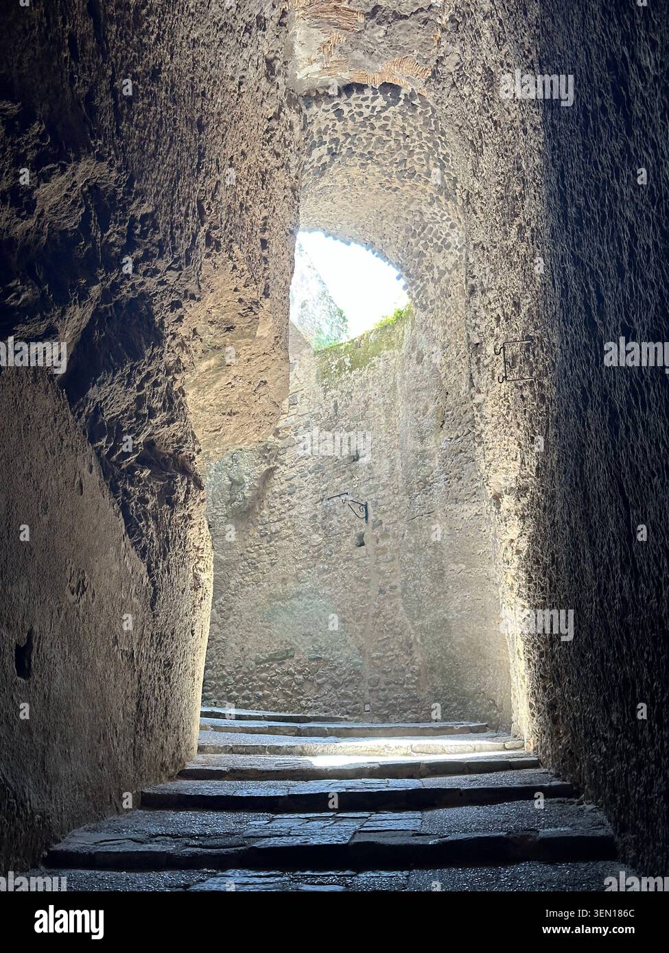 La luce del giorno si riversa attraverso un'apertura alta in un antico passaggio di pietra vuoto, illuminando gradini levigati dal tempo. - Immagine stock catturata con smartphone