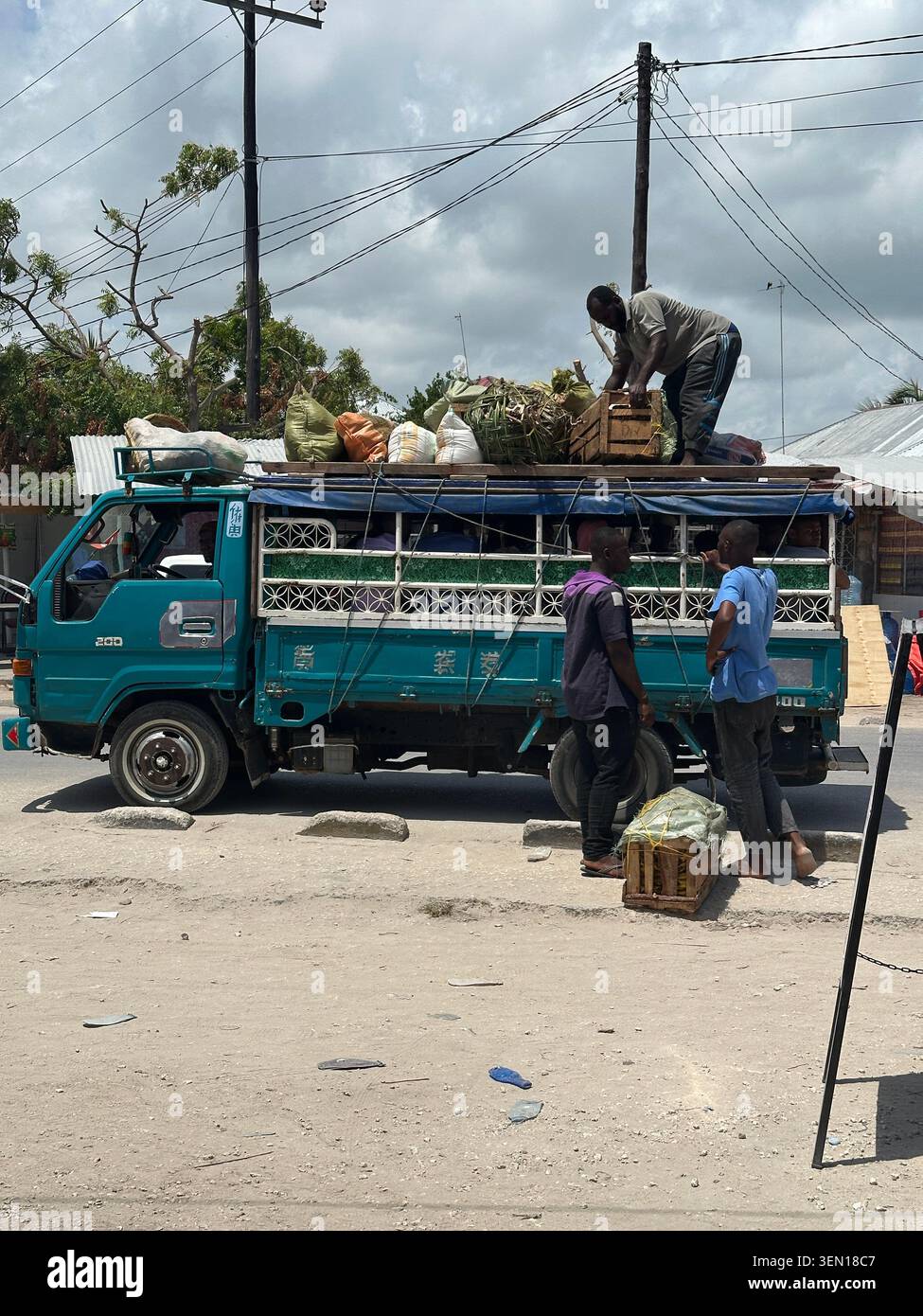 Un minibus pubblico decorato si ferma su una strada polverosa mentre le persone caricano bagagli e merci sul tetto. - Immagine stock catturata con smartphone