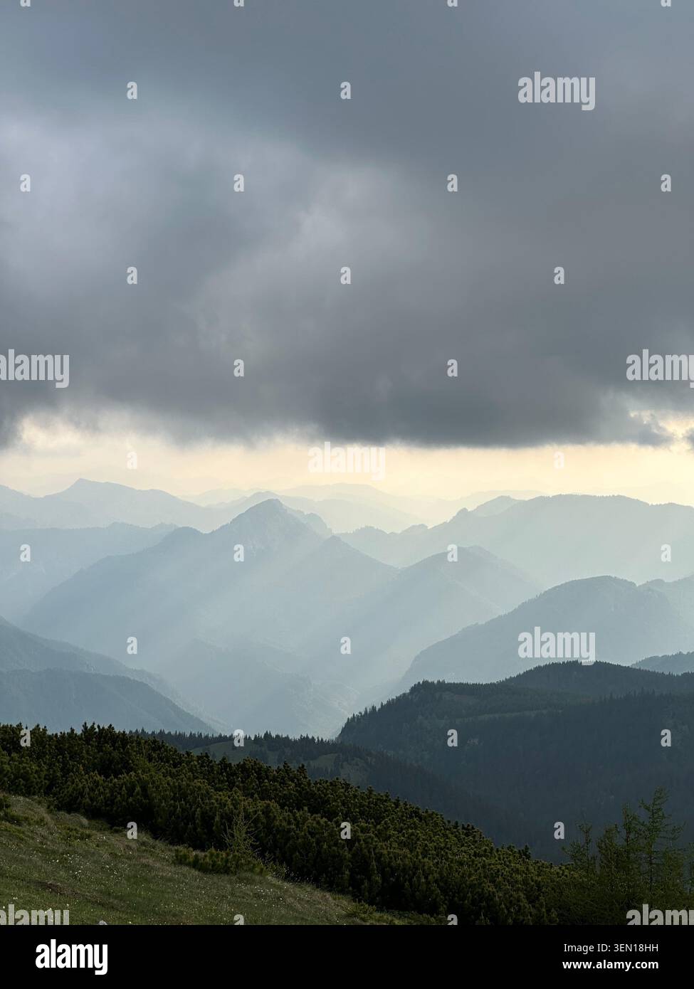 Nuvole tempestose scure premono sulle creste montuose stratificate mentre pale colonne di pioggia e luce attraversano la valle lontana. 1 - Immagine stock catturata con smartphone