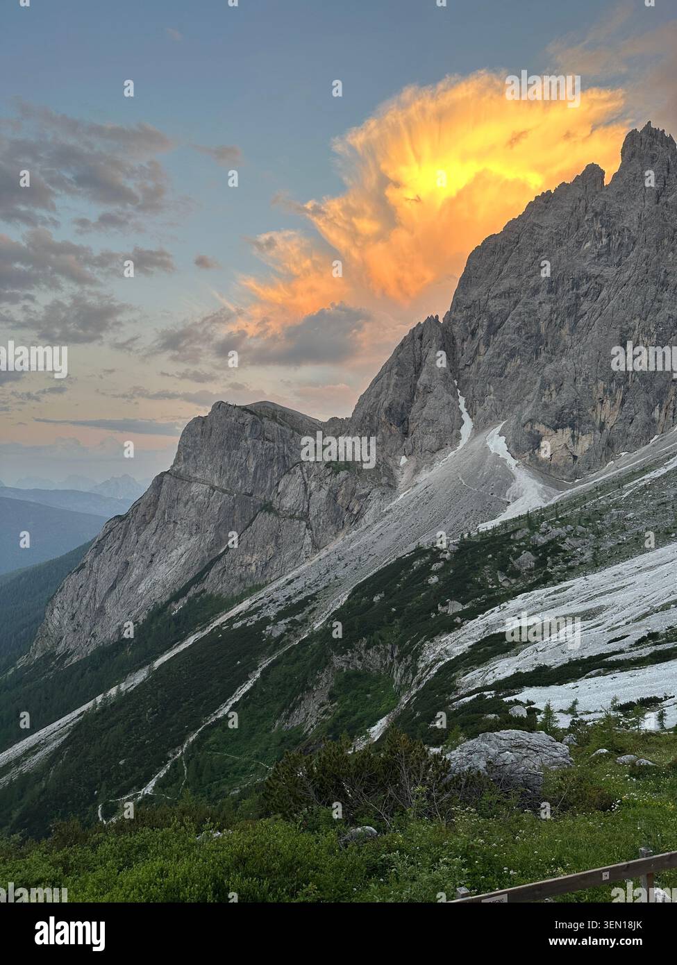 Una cresta di calcare cattura l'ultimo fuoco dorato del tramonto sopra i pendii alpini verdi e le strisce di neve persistente. - Immagine stock catturata con smartphone
