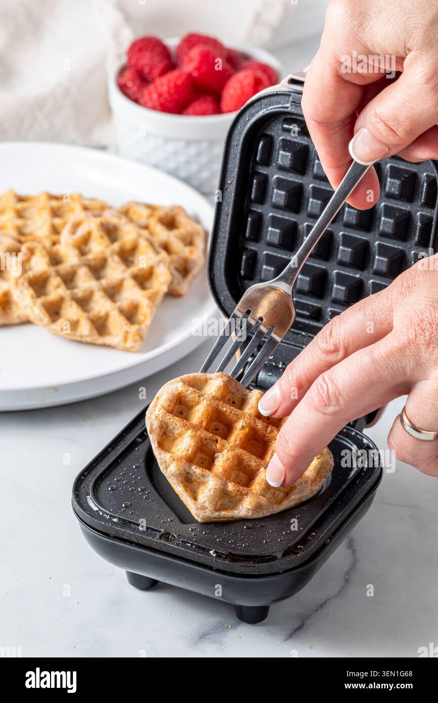 Un primo piano di una mano che rimuove i waffle appena fatti da una mini macchina per waffle. Foto Stock