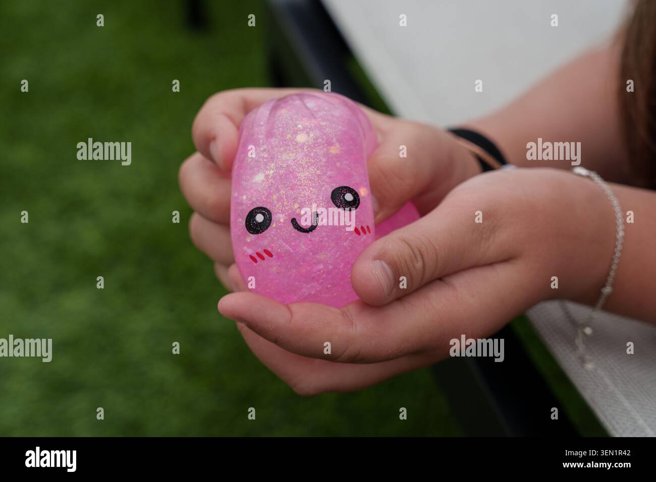 Primo piano di un bambino che stringe un giocattolo scintillante rosa con il viso sorridente, mettendo in risalto il gioco sensoriale, il relax e la stimolazione tattile Foto Stock