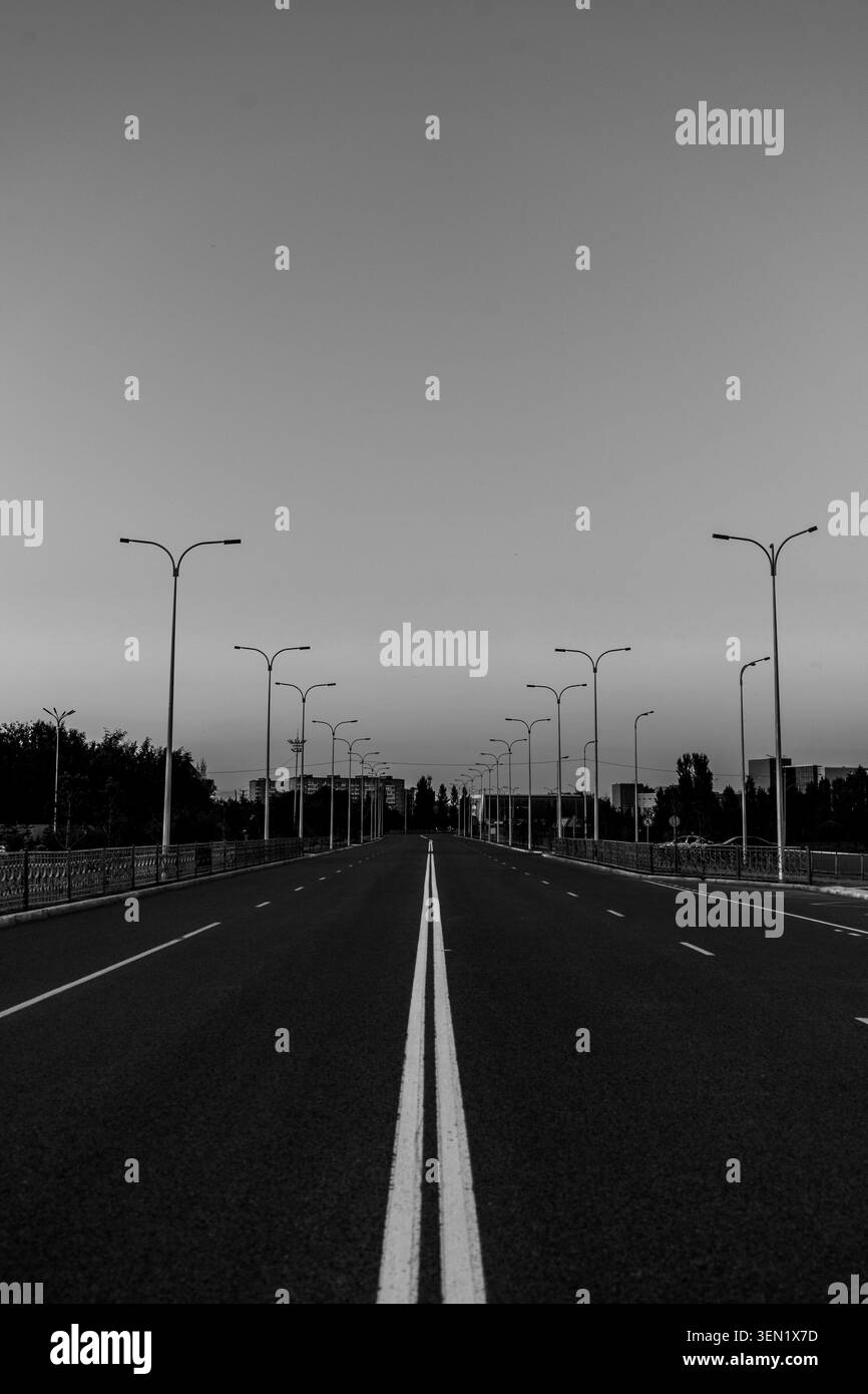 Fotografia in bianco e nero di una strada rettilinea che si estende all'orizzonte. Linee pulite, linee di demarcazione e asfalto vuoto, nessuno. Minimalista da viaggio o jo Foto Stock