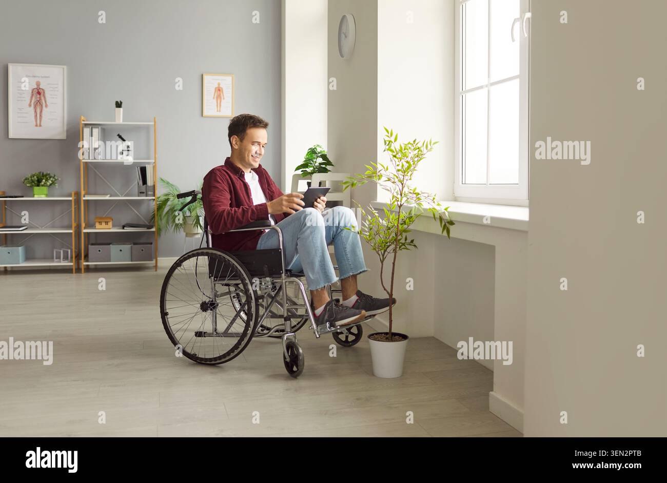 Giovane felice in sedia a rotelle che utilizza un tablet digitale e si diverte con le comunicazioni e l'intrattenimento online. Foto Stock