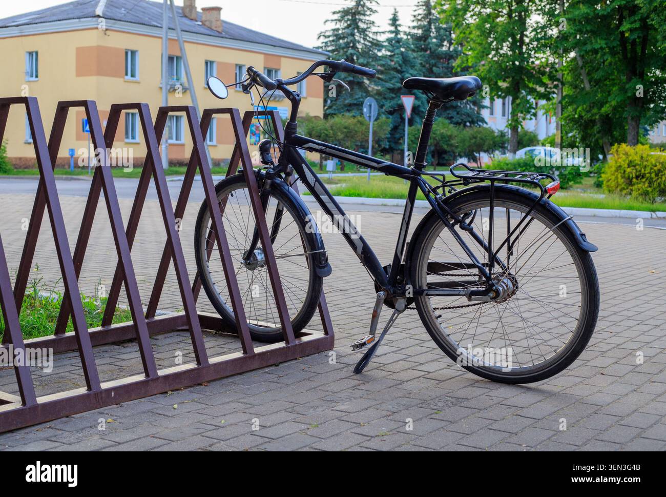 Cavalletti per biciclette classici neri fissati a un portabiciclette marrone in metallo sul marciapiede della città. Parcheggio urbano ecologico vicino al marciapiede Foto Stock
