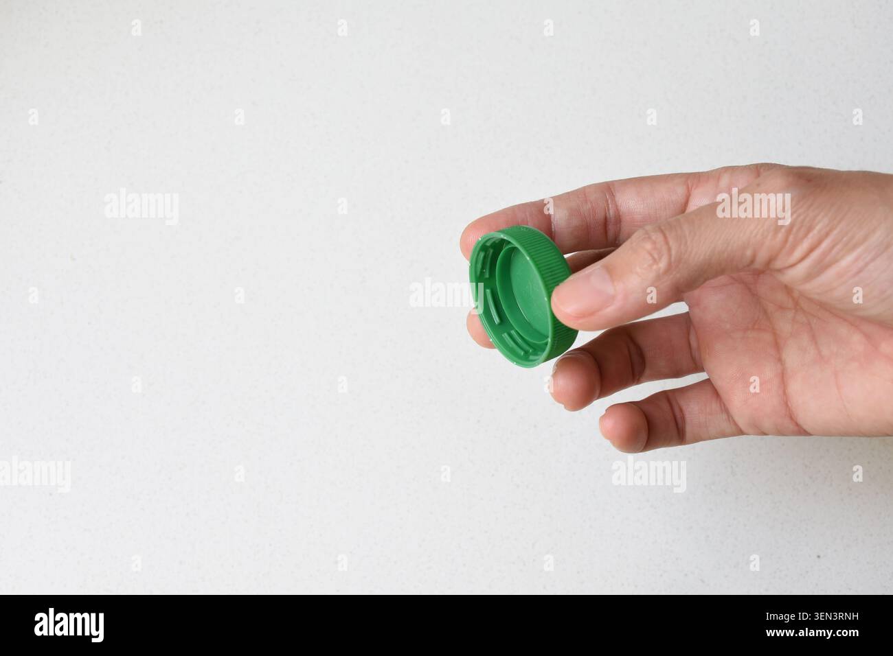 Vista dall'alto di una mano umana con tappo verde isolato su uno sfondo bianco pulito. Ideale per confezionamento, riciclaggio, sostenibilità, bevande Foto Stock