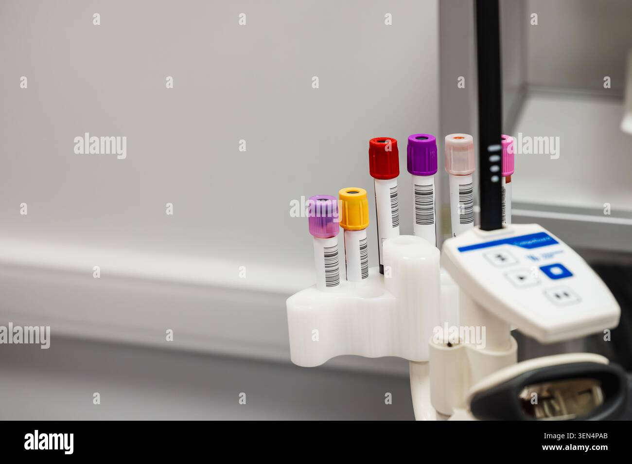 Primo piano di provette per campioni di sangue con tappo colorato in un supporto accanto a un analizzatore in una clinica per donazioni di sangue, illustrando l'analisi del sangue di laboratorio e l'analisi sc Foto Stock
