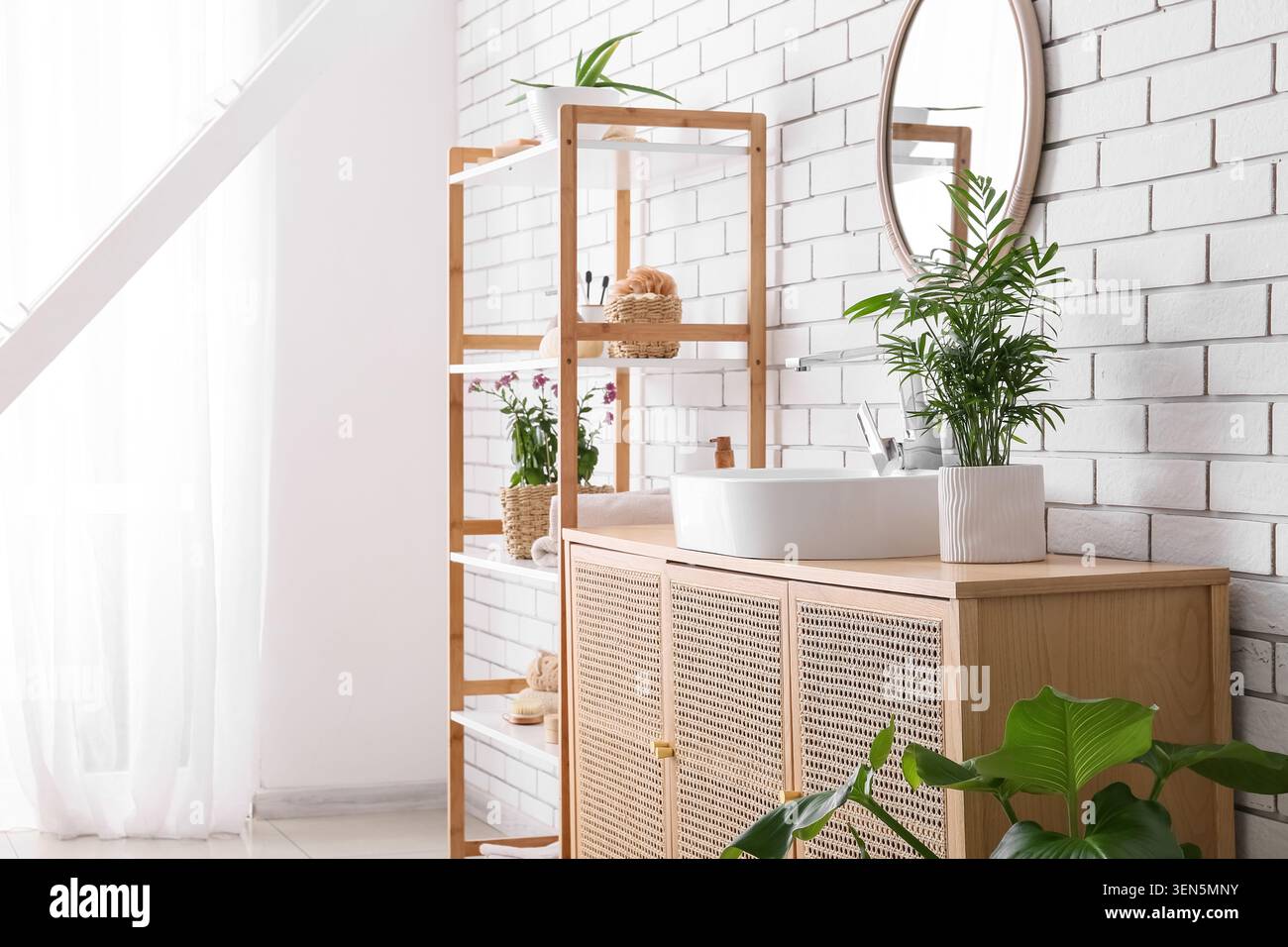 Bagno dal design moderno con pareti in mattoni bianchi, lavandino in legno, specchio rotondo e piante verdi Foto Stock
