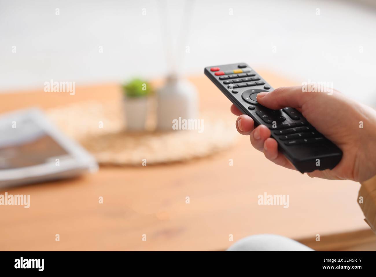 Tenendo a mano il telecomando nero per la televisione o il dispositivo multimediale, l'Home Entertainment e la tecnologia moderna, la scena suggerisce svago e convenienza Foto Stock