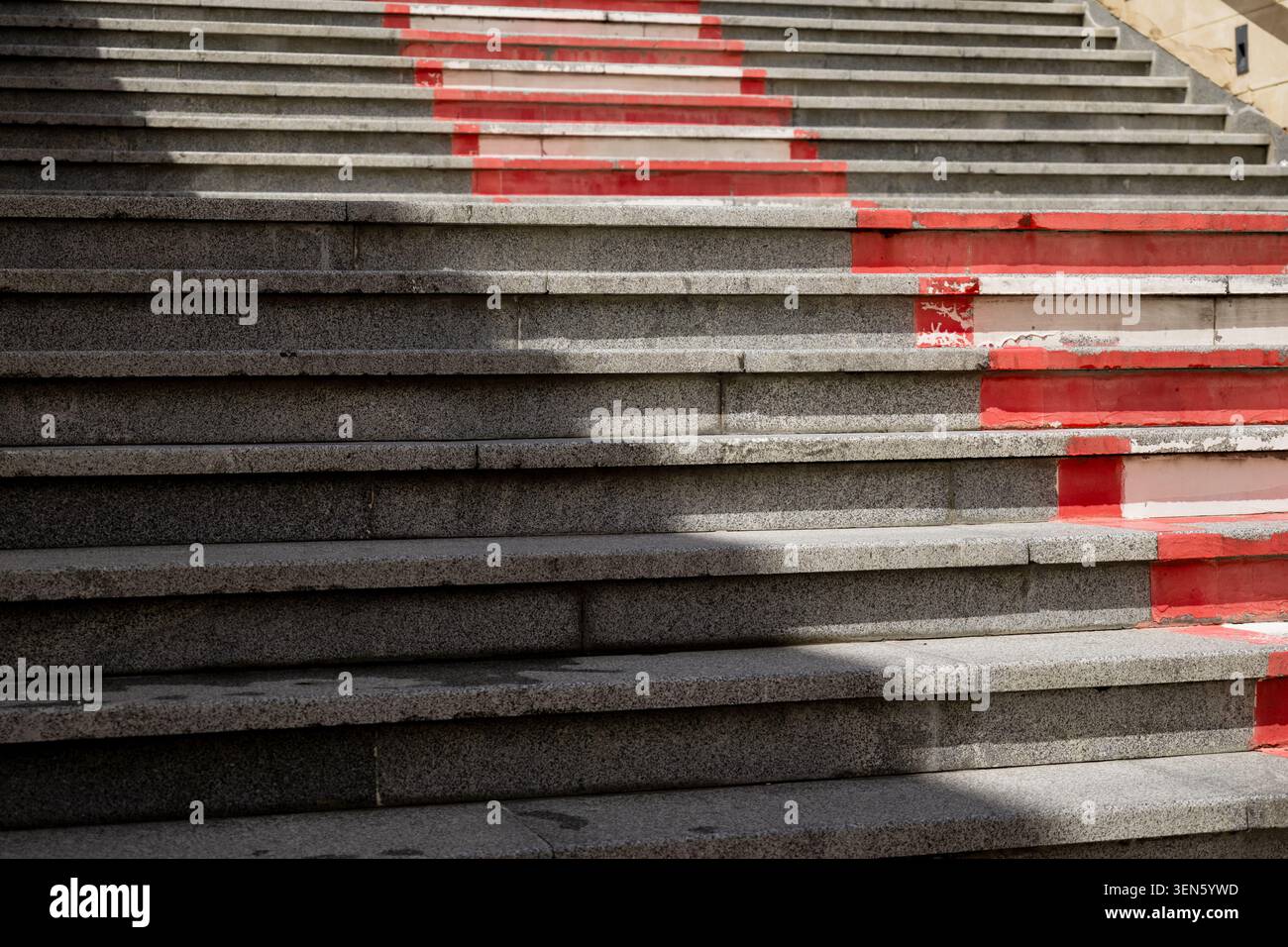 Vista a trama dei gradini di granito contrassegnati da una linea di avvertimento rossa resistente agli agenti atmosferici e da un'ombra dura Foto Stock