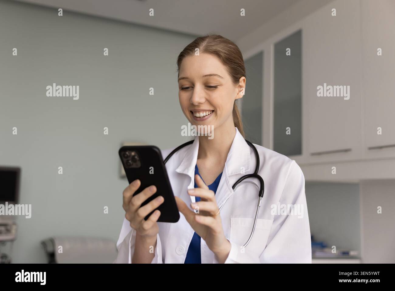 Medico sorridente si trova in clinica sala esame controllare smartphone Foto Stock