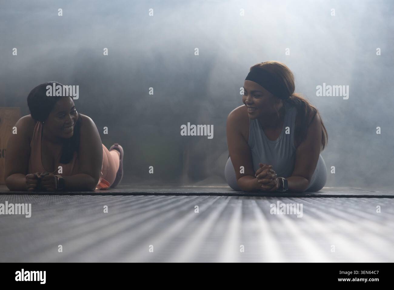 Amiche afroamericane che tengono tavole dell'avambraccio su tappetini da palestra testurizzati con fascia e orologio Foto Stock