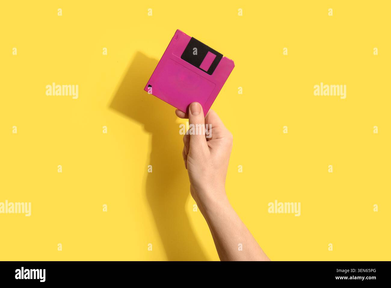 Mano che tiene il disco floppy rosa su sfondo giallo, tecnologia retro e concetto di archiviazione dati, trasferimento digitale di informazioni Foto Stock