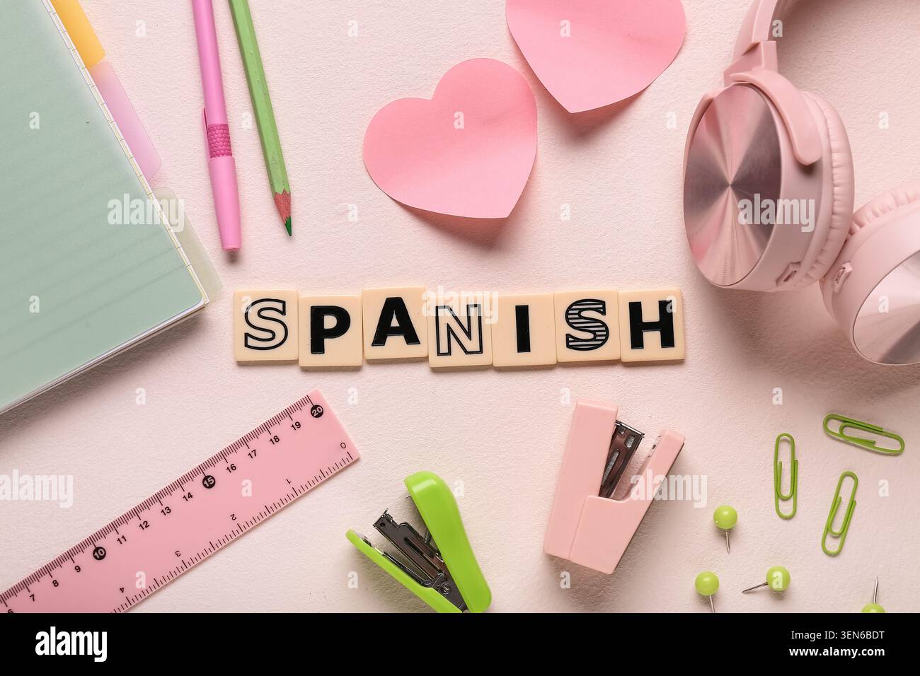 Apprendimento della lingua spagnola con cancelleria, cuffie e piastrelle pieghevoli su sfondo rosa Foto Stock