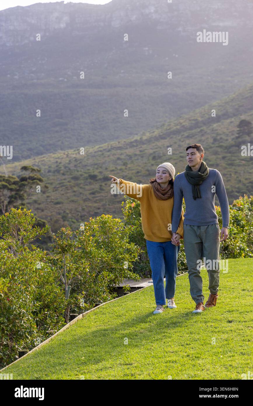 Coppia asiatica con foulard che cammina su una sporgenza erbosa che punta verso una cresta distante, copia spazio Foto Stock