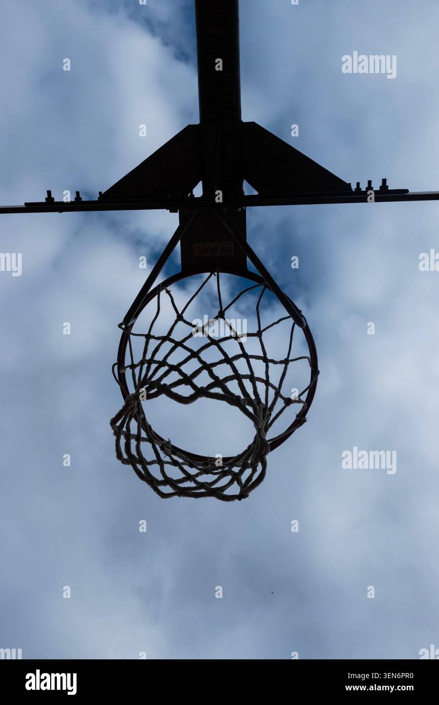 Vista ad angolo basso di un canestro da basket all'aperto e silhouette a rete su un cielo blu nuvoloso Foto Stock