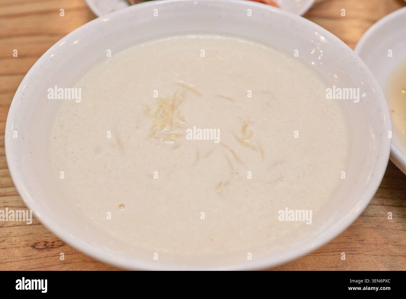 Una ciotola bianca piena di cremoso brodo beige di latte di soia offre un pasto estivo minimalista, mentre le bacchette sollevano sottili corde di frumento mostrando un'eccellenza pura Foto Stock