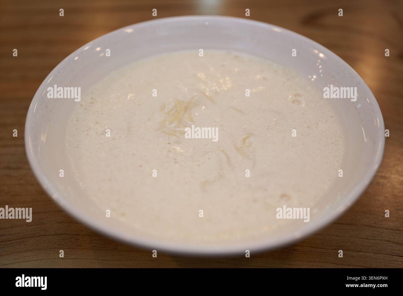 Una ciotola bianca piena di cremoso brodo beige di latte di soia offre un pasto estivo minimalista, mentre le bacchette sollevano sottili corde di frumento mostrando un'eccellenza pura Foto Stock