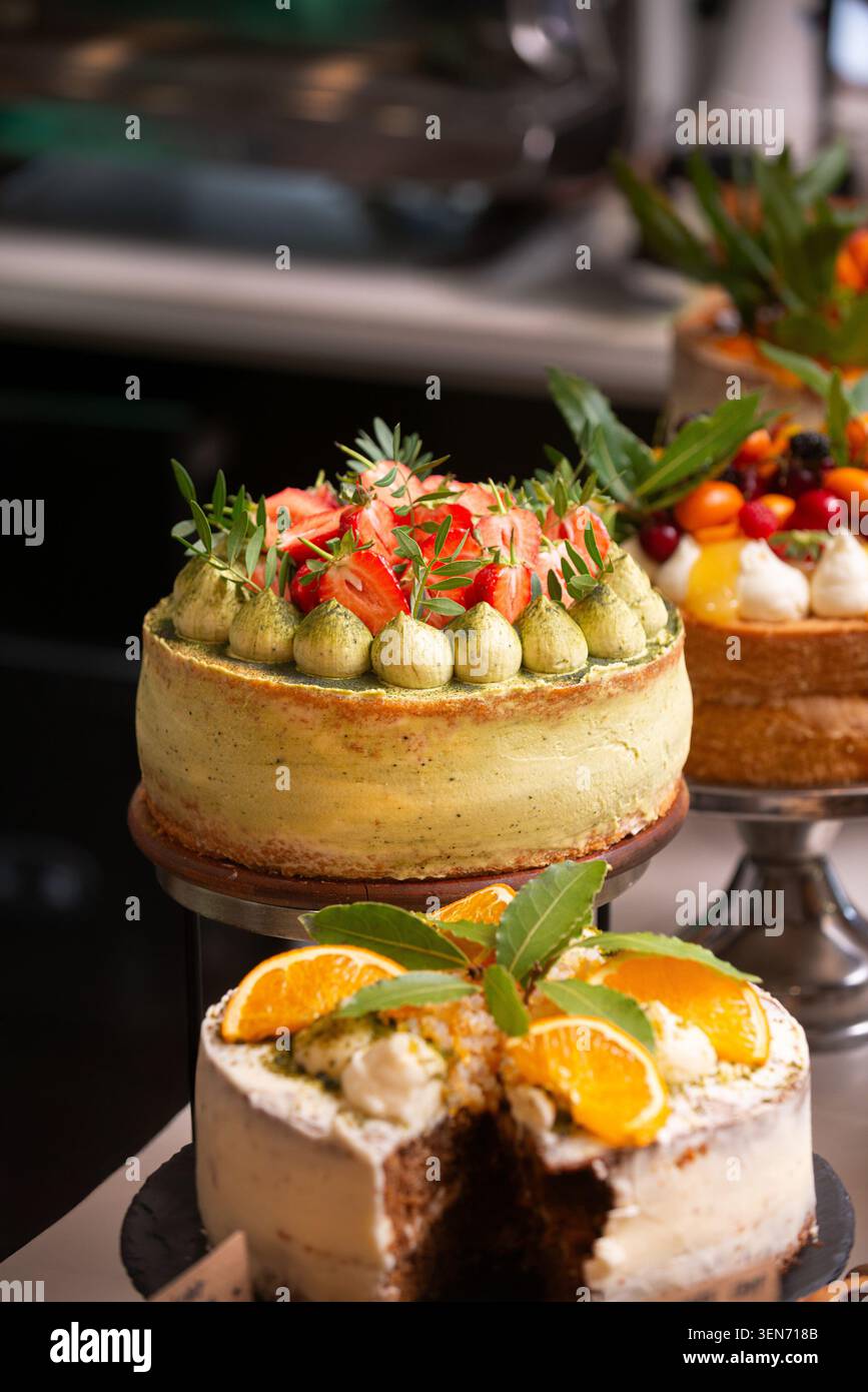 Primo piano di torte artigianali su banchi, con una torta di fragole matcha e una torta all'arancia affettata. Foto Stock