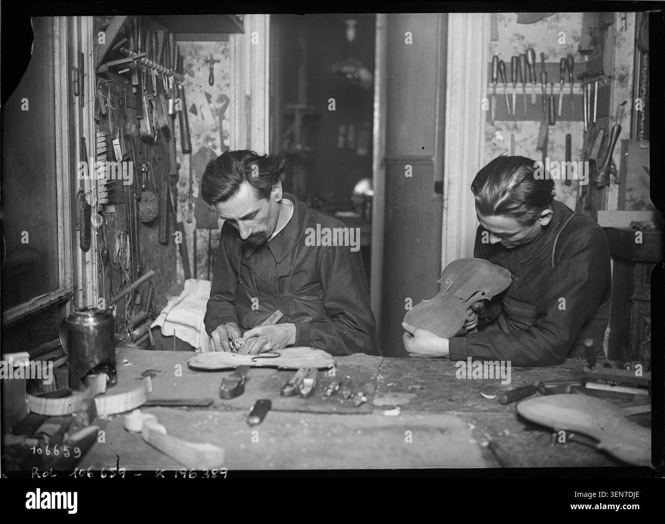 Una fotografia del 1926 di Agence Rol registra i liutai al lavoro in un'officina di liuteria, impegnati nella fabbricazione o nella riparazione. L'immagine documenta le pratiche tecniche e l'ambiente artigianale in Francia. Foto Stock